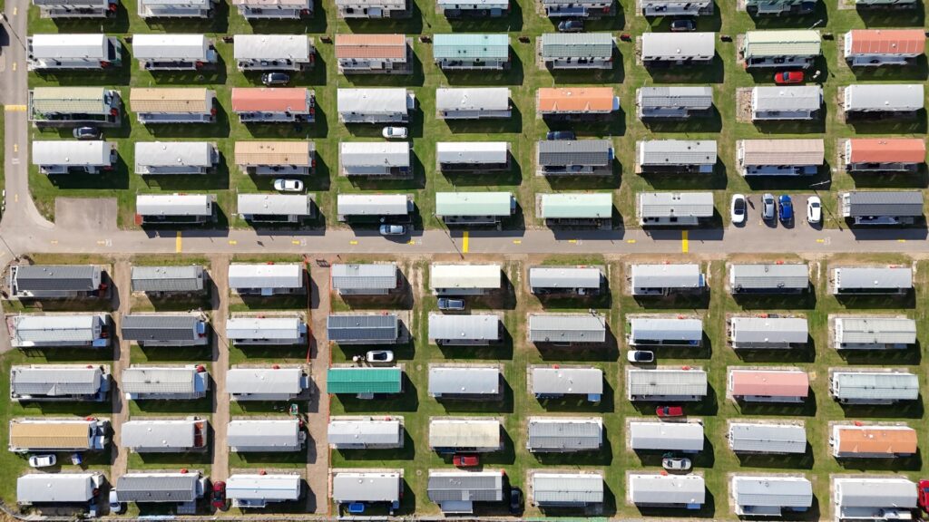 Aerial view of a densely arranged mobile home community with rows of rectangular homes separated by narrow roads and green lawns.