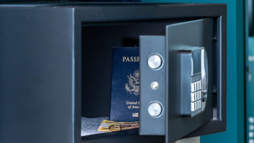 An open dark metal electronic safe containing a U.S. passport, money, and a ring.