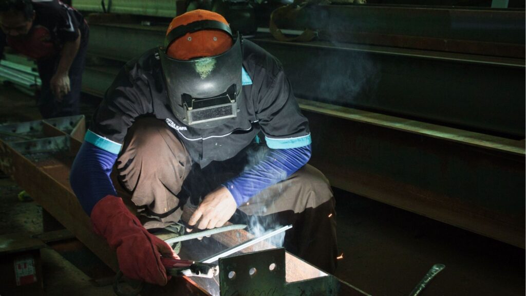 Industrial welder with a torch and protective helmet.