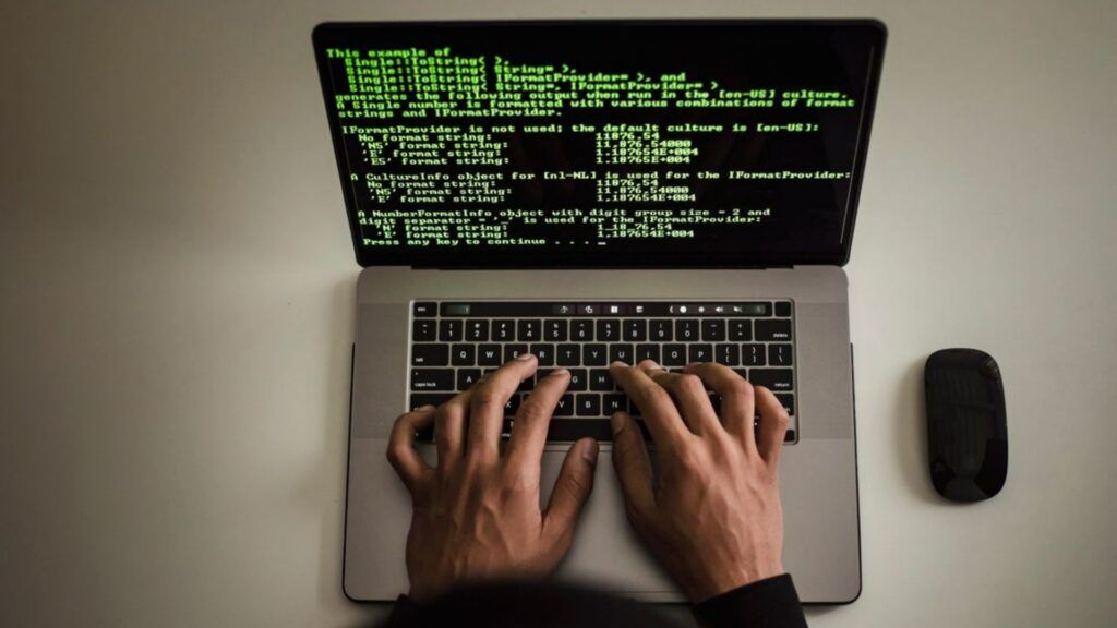 Hands typing code on a laptop with programming text on screen.