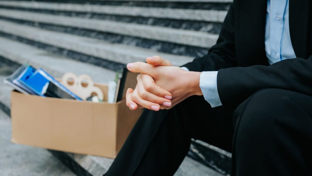 Person in a suit sitting on steps with a box of belongings after being let go.
