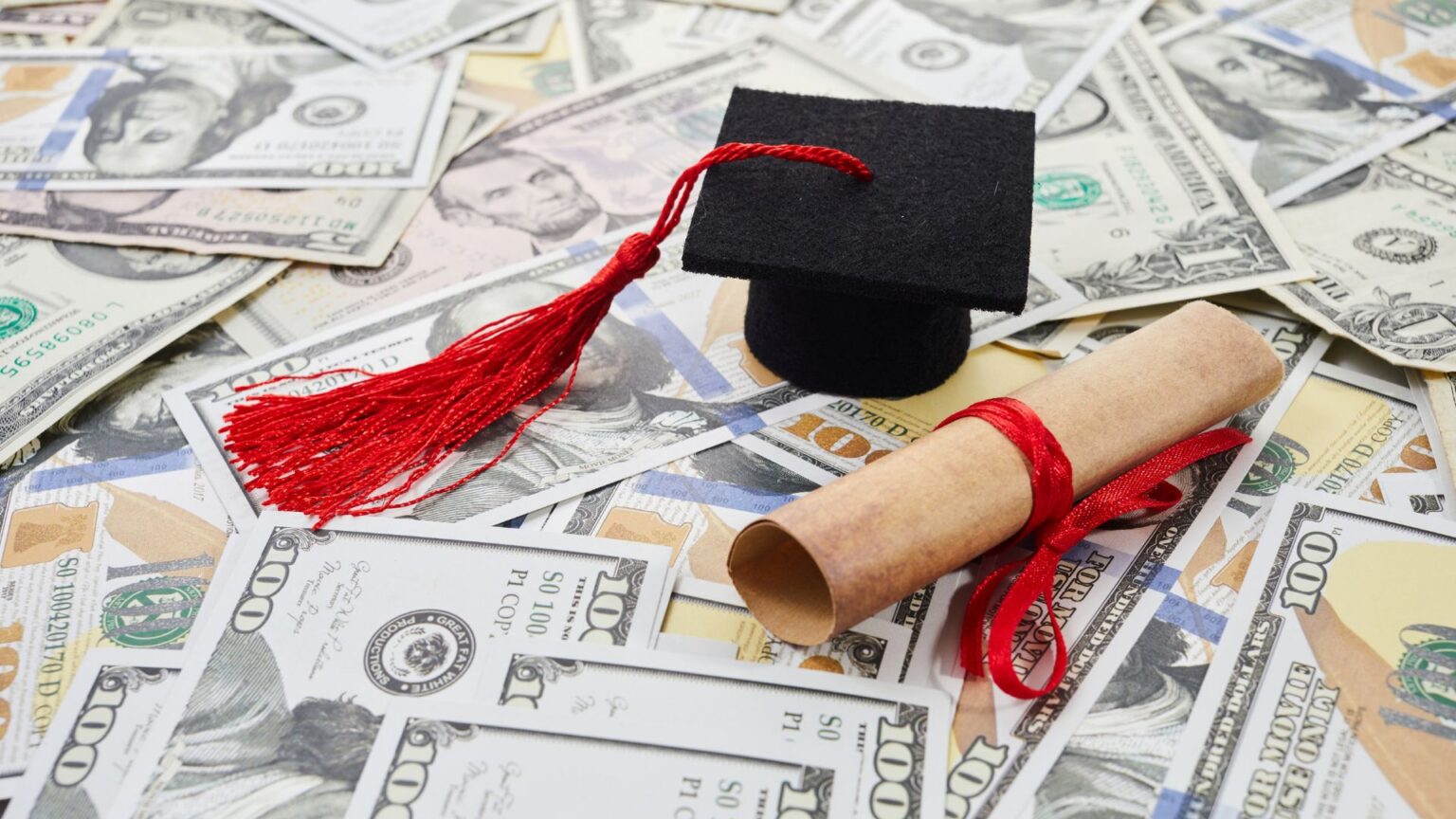 1 in 5 Student Loan Borrowers Is Now in Default as Payment Struggles Grow Graduation cap and diploma resting on cash.