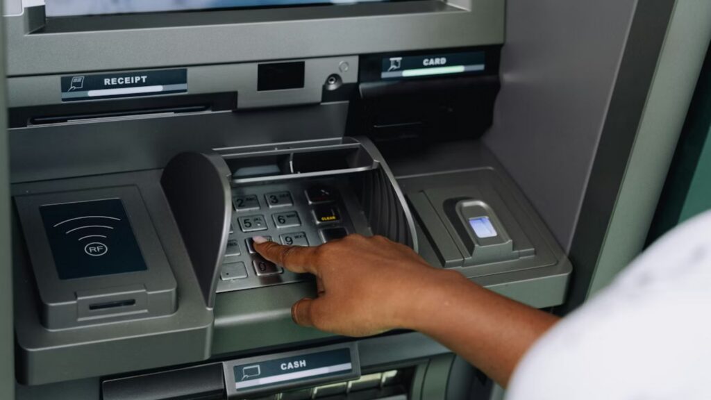 A close-up of a person's hand on the keypads of an ATM.
