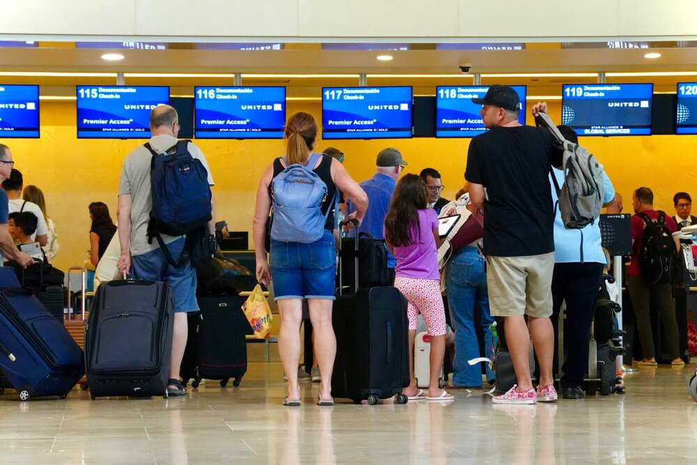 Travelers waiting in line with luggage at United Airlines airport check-in counters.